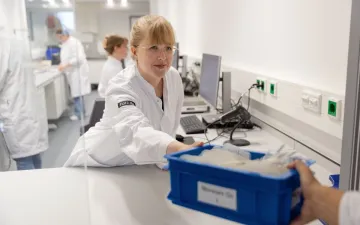 Medewerker in labjas pakt een plastic bak met bloedproducten aan van een collega