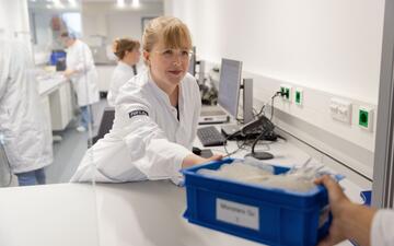 Medewerker in labjas pakt een plastic bak met bloedproducten aan van een collega