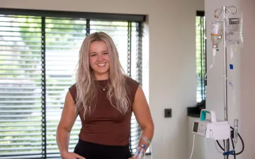Jonge vrouw staat met plasma-infuus voor een raam