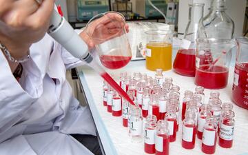 Foto van een laboratoriumtafel met kleine flesjes. Een hand met een pipet vult de flesjes. 