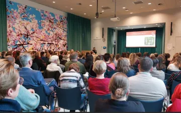 Foto van een conferentiezaal met mensen op de rug gezien. 