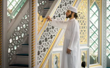 Foto van Faried in een moskee. Hij is gekleed in een witte djeballa en draagt een witte kufi