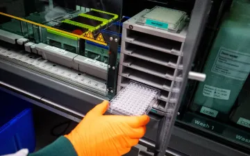 Laboratoriummedewerker van Sanquin plaatst een microtiterplaat in analyseapparatuur voor coronagerelateerd bloedonderzoek