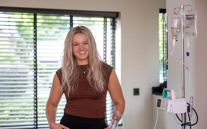 Jonge vrouw staat met plasma-infuus voor een raam
