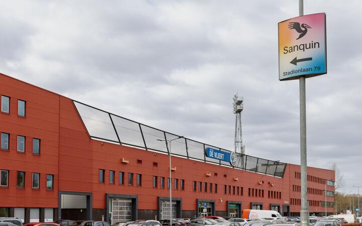 Foto van het voetbalstadion in Den Bosch. Op de voorgrond een verkeersbord met daarop het logo van Sanquin. 