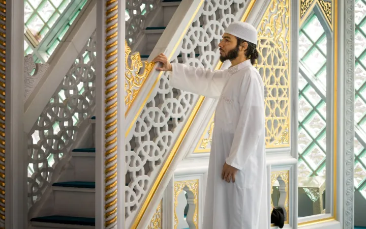 Foto van Faried in een moskee. Hij is gekleed in een witte djeballa en draagt een witte kufi