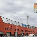 Foto van het voetbalstadion in Den Bosch. Op de voorgrond een verkeersbord met daarop het logo van Sanquin. 