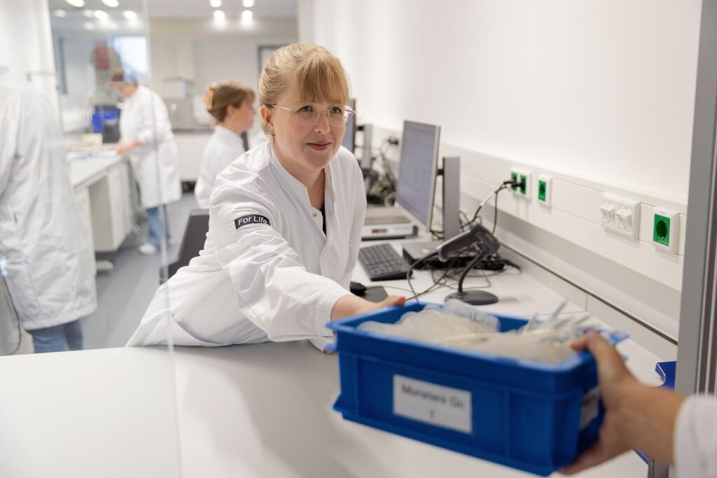 Medewerker in labjas pakt een plastic bak met bloedproducten aan van een collega
