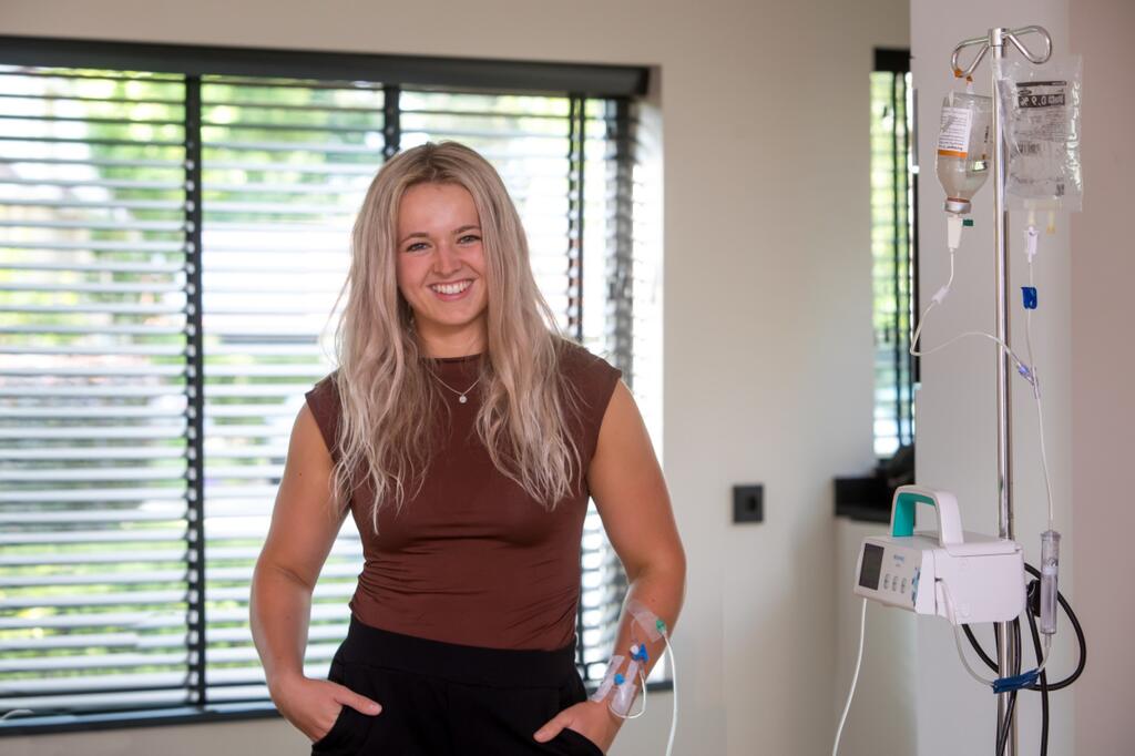 Jonge vrouw staat met plasma-infuus voor een raam