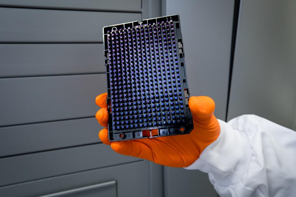 Foto van een hand in oranje handschoen die de nieuwe bloedgroepentest vasthoud tegen een grijze achtergrond.