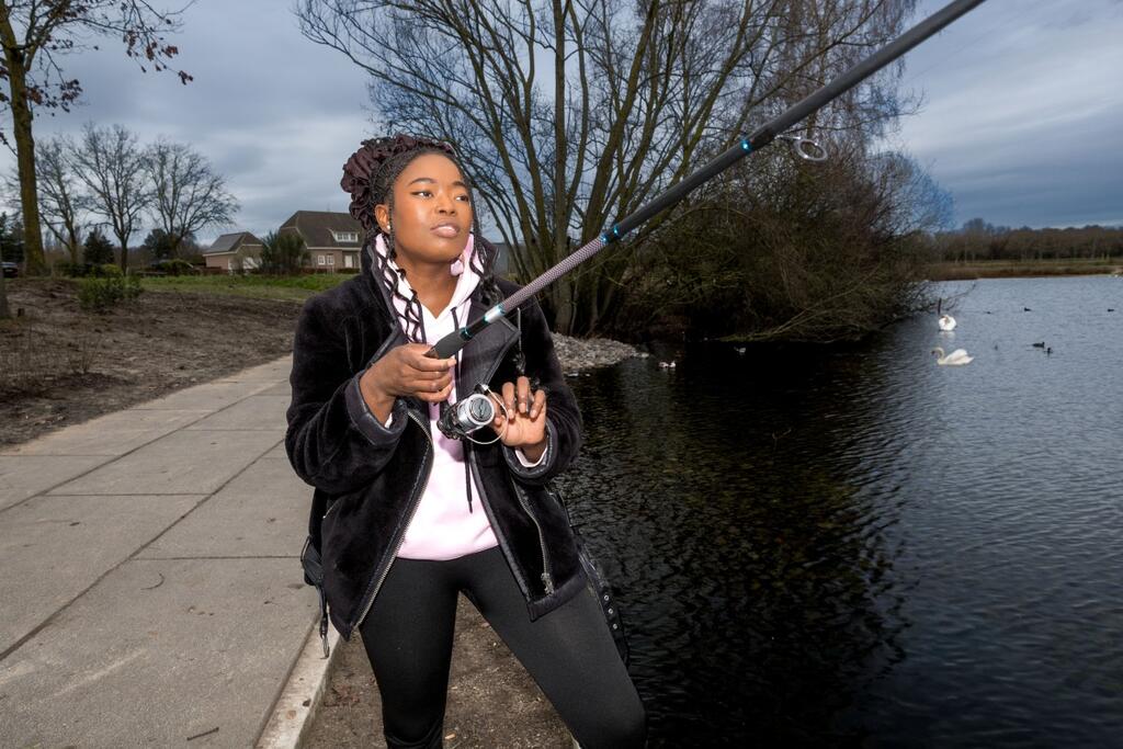 Foto van vrouw met hengel aan de waterkant in landelijke omgeving