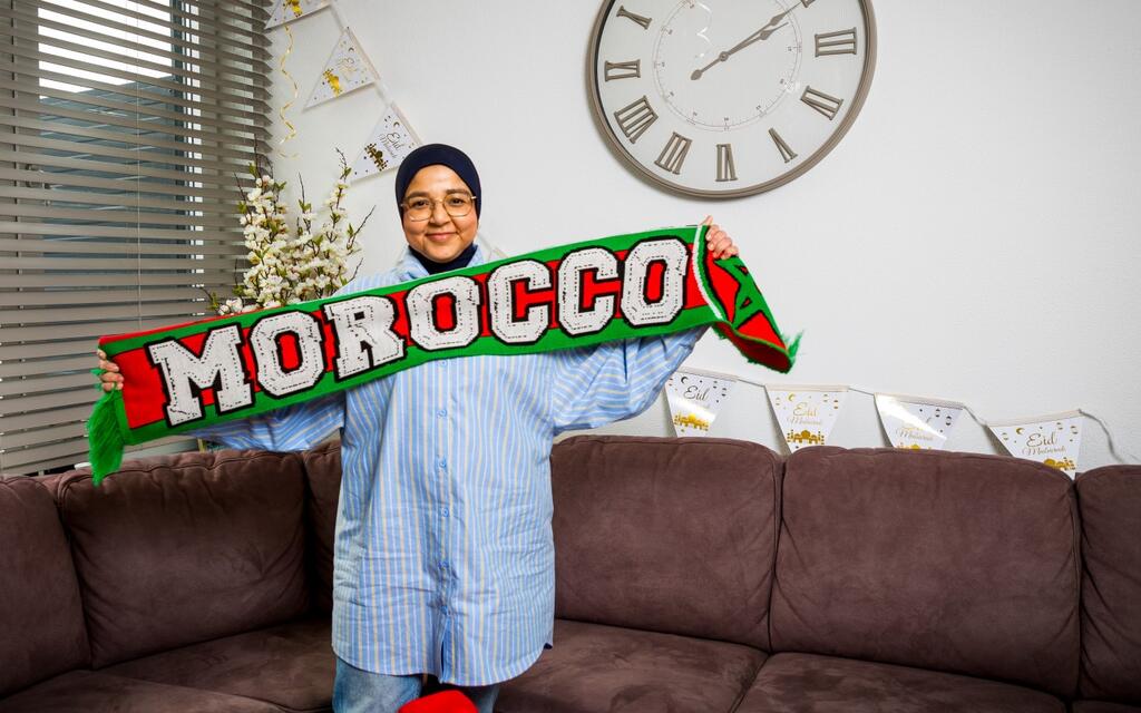 Foto can Chaymaa in haar woonkamer, in haar hand een voetbalsjaal 'Morocco' en slingers Eid Mubarak aan de muur