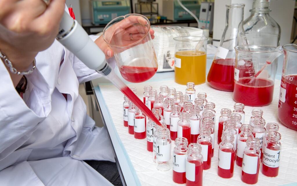 Foto van een laboratoriumtafel met kleine flesjes. Een hand met een pipet vult de flesjes. 