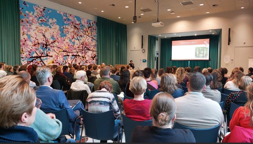 Foto van een conferentiezaal met mensen op de rug gezien. 