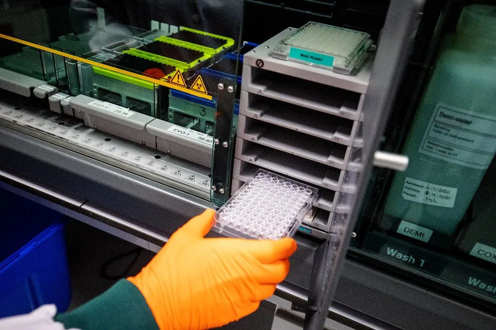 Laboratoriummedewerker van Sanquin plaatst een microtiterplaat in analyseapparatuur voor coronagerelateerd bloedonderzoek