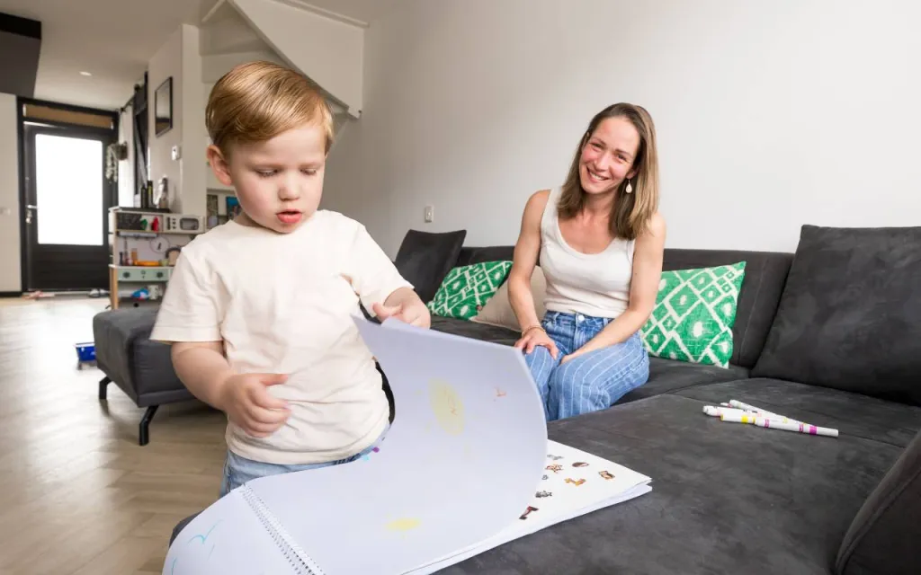 Zoontje Levi met een tekenboek, ouder Veronique lacht op de achtergrond