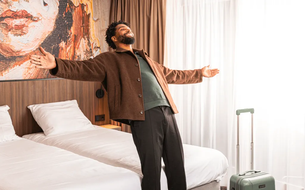Gast laat zich ontspannen achterover vallen op het bed in een hotelkamer met twee bedden