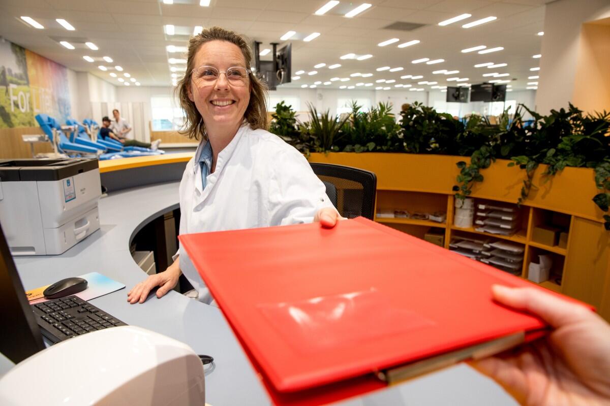 Medewerker aan de balie overhandigd lachend een rode map met de medische vragenlijst